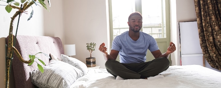 A person meditates while sitting on their bed.