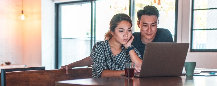 Two people sit together at a table and look at a laptop.