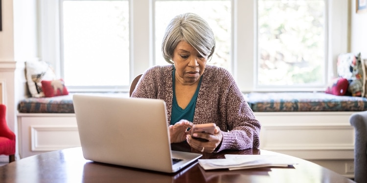 A person sitting in front of their laptop and typing on their phone.