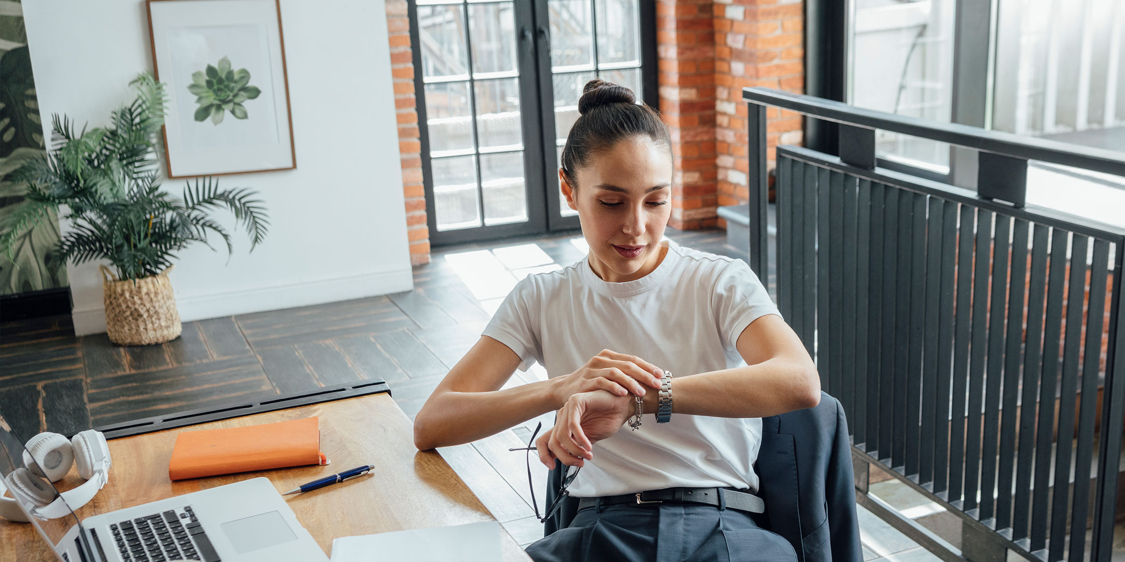 A person sitting at a desk looking at their watch to check the date and estimate when they should expect a tax refund.