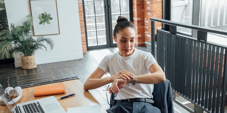 A person sitting at a desk looking at their watch to check the date and estimate when they should expect a tax refund.