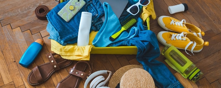 Suitcase overflowing with vacation clothes and accessories.