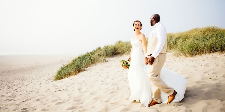 A married couple walk on the beach.