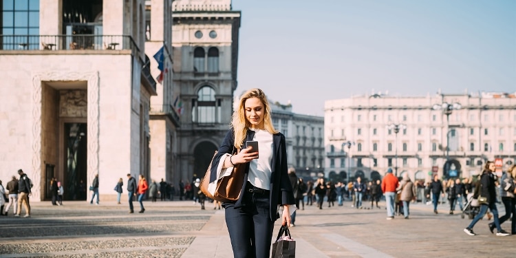 A smiling person traveling abroad and looking at their cellphone while walking outside.