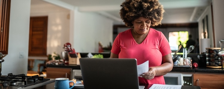 Person holding papers stands at a computer and prepares for a credit check that will accompany her credit card application.