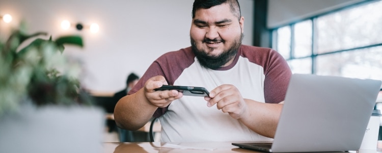 A person sits in front of their computer. They deposit their paycheck using a mobile app.
