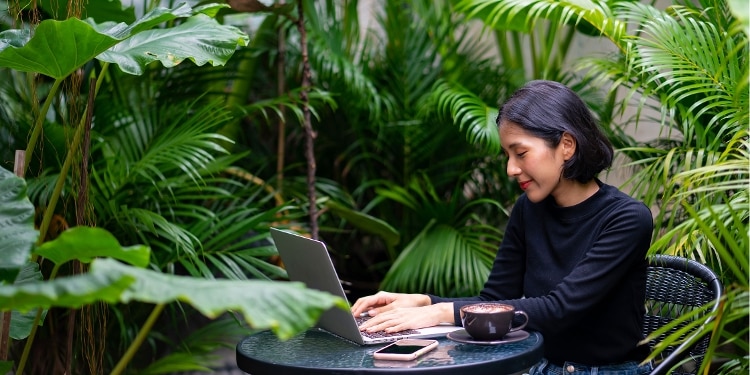 A person sitting at a table surrounded by green plants uses their laptop to check their credit limit.