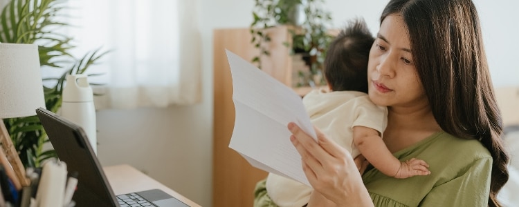 A parent holds their baby while they review their paper bank statement.