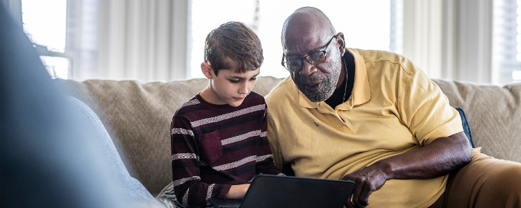 Adult and child sitting on the couch and looking at a laptop.