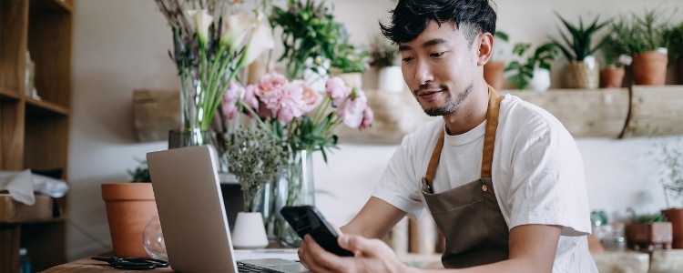 A person sits at the counter of a plant shop and pays a bill online with their phone.
