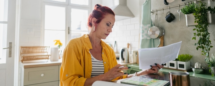 A person sits at a table while holding papers and looking at a tablet to calculate their taxable income.