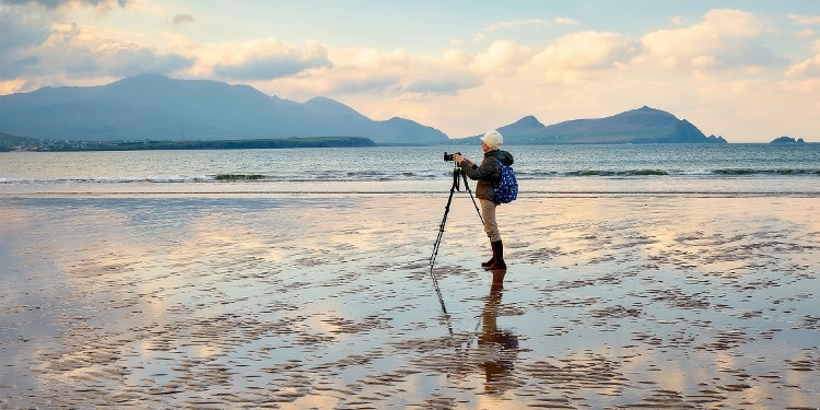 A person uses a tripod to take photos on a wide, empty beach.