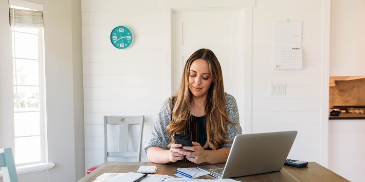 A woman using her phone while sitting in front of her laptop.