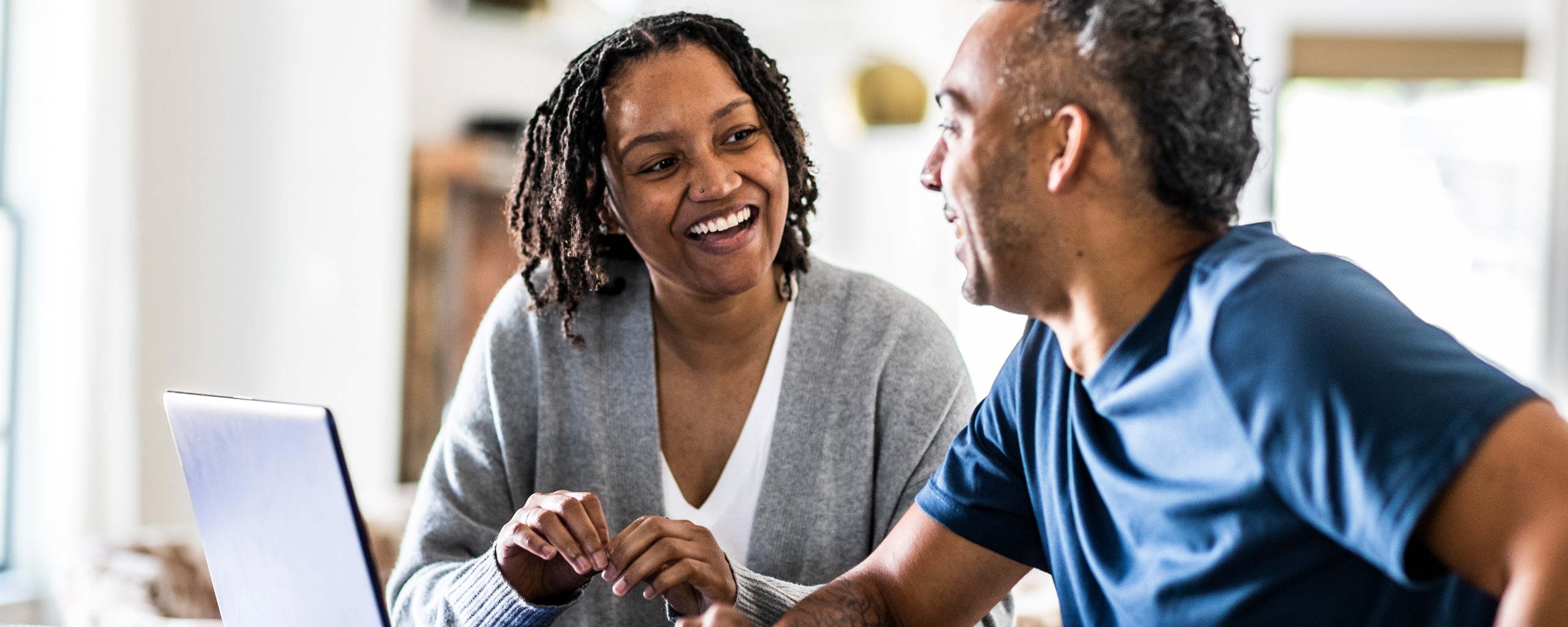 Smiling couple discussing Roth IRAs and their retirement while sitting down with their laptop.