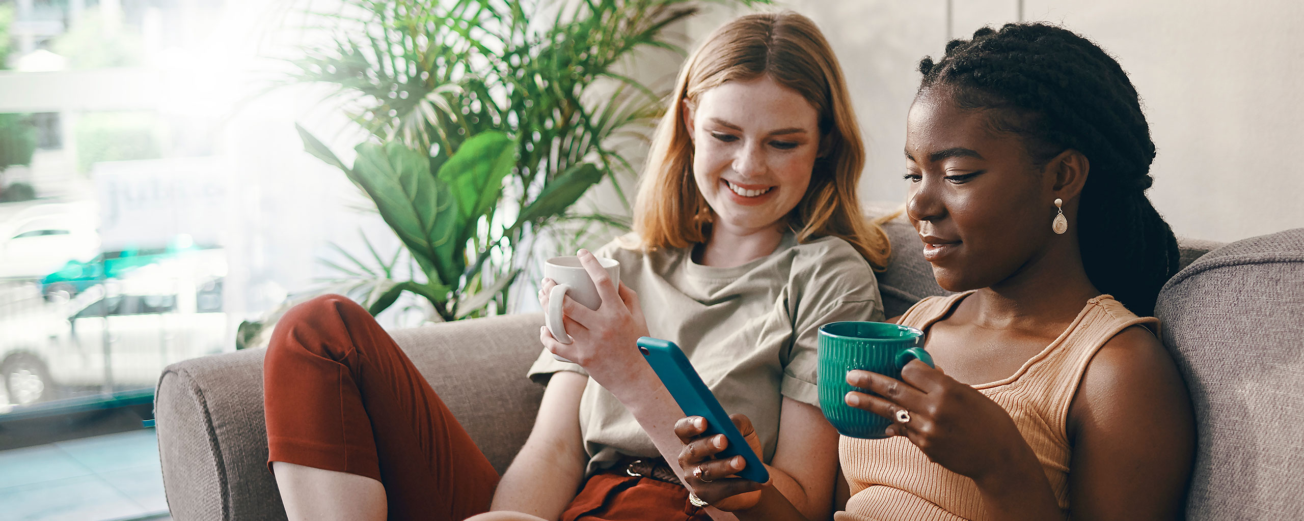 Two people sitting on a couch and drinking coffee while looking at credit scores on a cellphone.