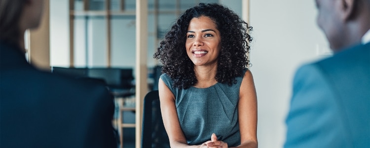 A person dressed in business attire sits at a conference table across from two other business professionals.