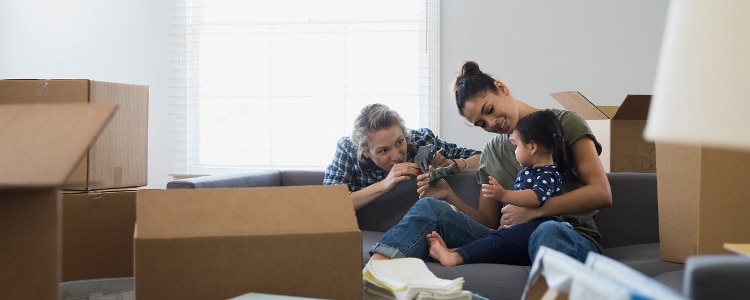 A couple plays with their child in their new rental home among moving boxes.
