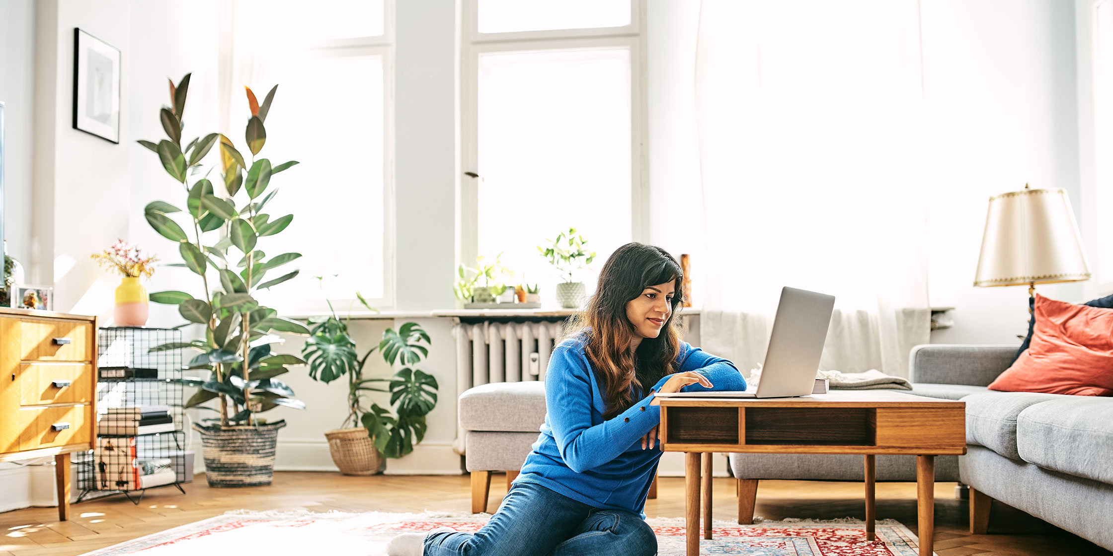 A person sitting next to a table looks at an open laptop.
