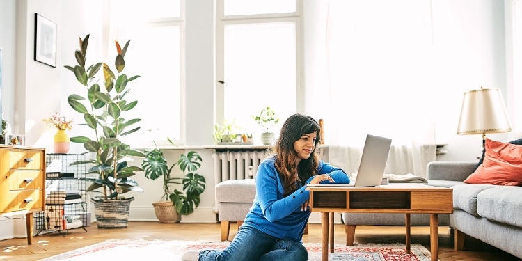 A person sitting next to a table looks at an open laptop.
