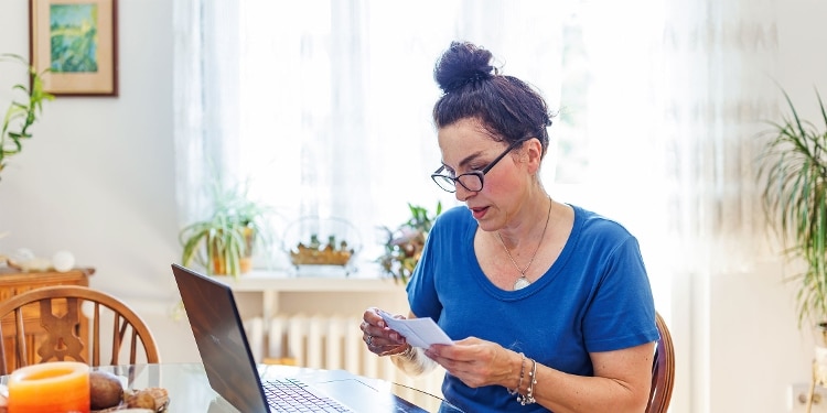 A person in glasses working on their laptop at their kitchen table.