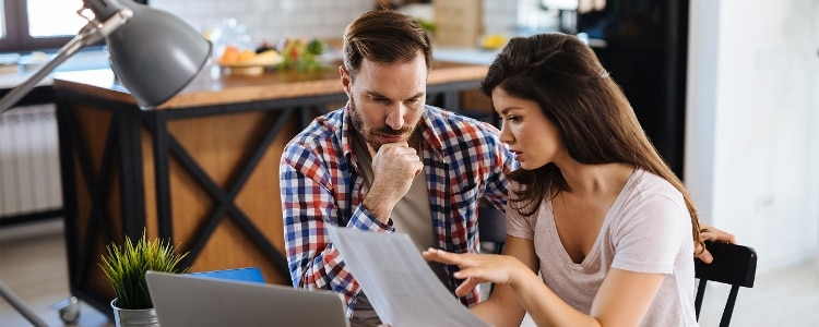 Two people look at information related to their finances while sitting in front of a laptop.