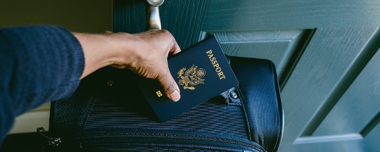 A photo of a person holding their U.S. passport and carrying a suitcase.