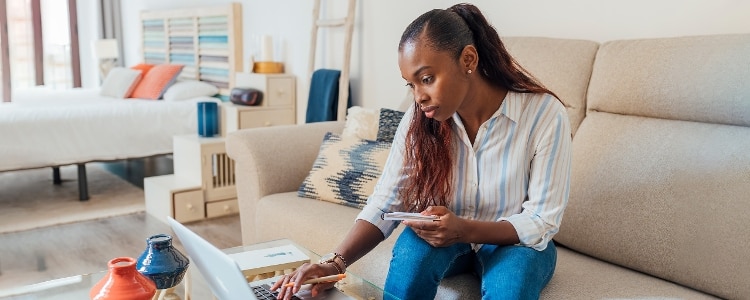 A woman sits on a couch and uses her laptop to research wire transfers.