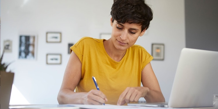 A person fills out a money order while sitting at their home desk.