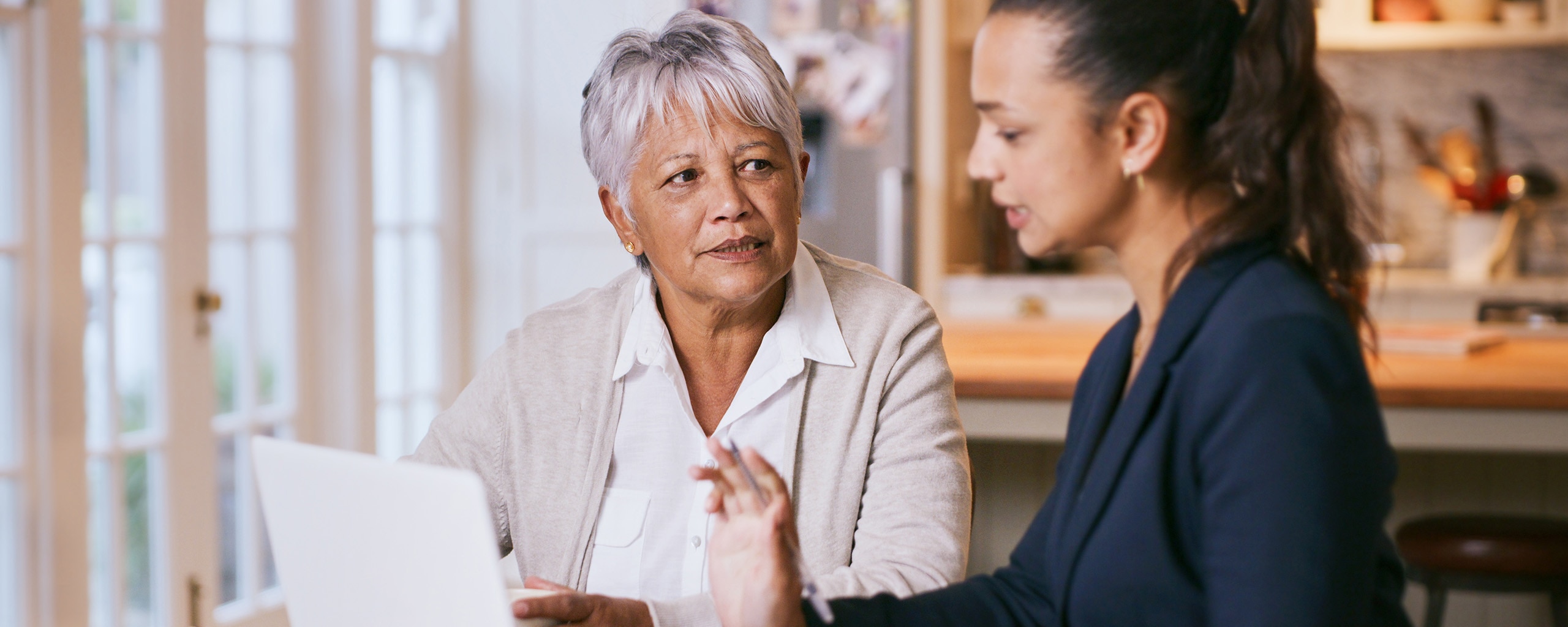An older and a younger person discuss debt while using a laptop at home.