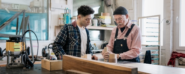 A student observes while a technician explains woodworking techniques