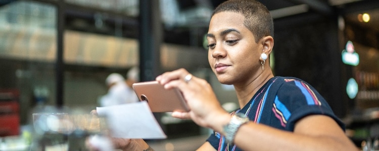 A young person deposits a check using their phone while sitting in a cafe.
