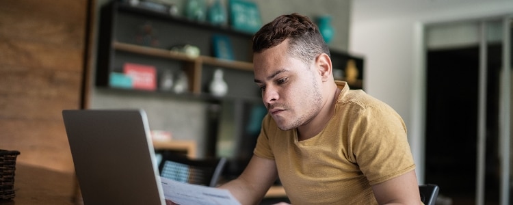 A young person looking at their laptop while holding a credit card application.