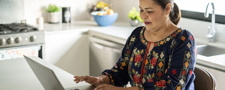 A photo of a person in their kitchen, using their laptop to research how to cash in a savings bond.