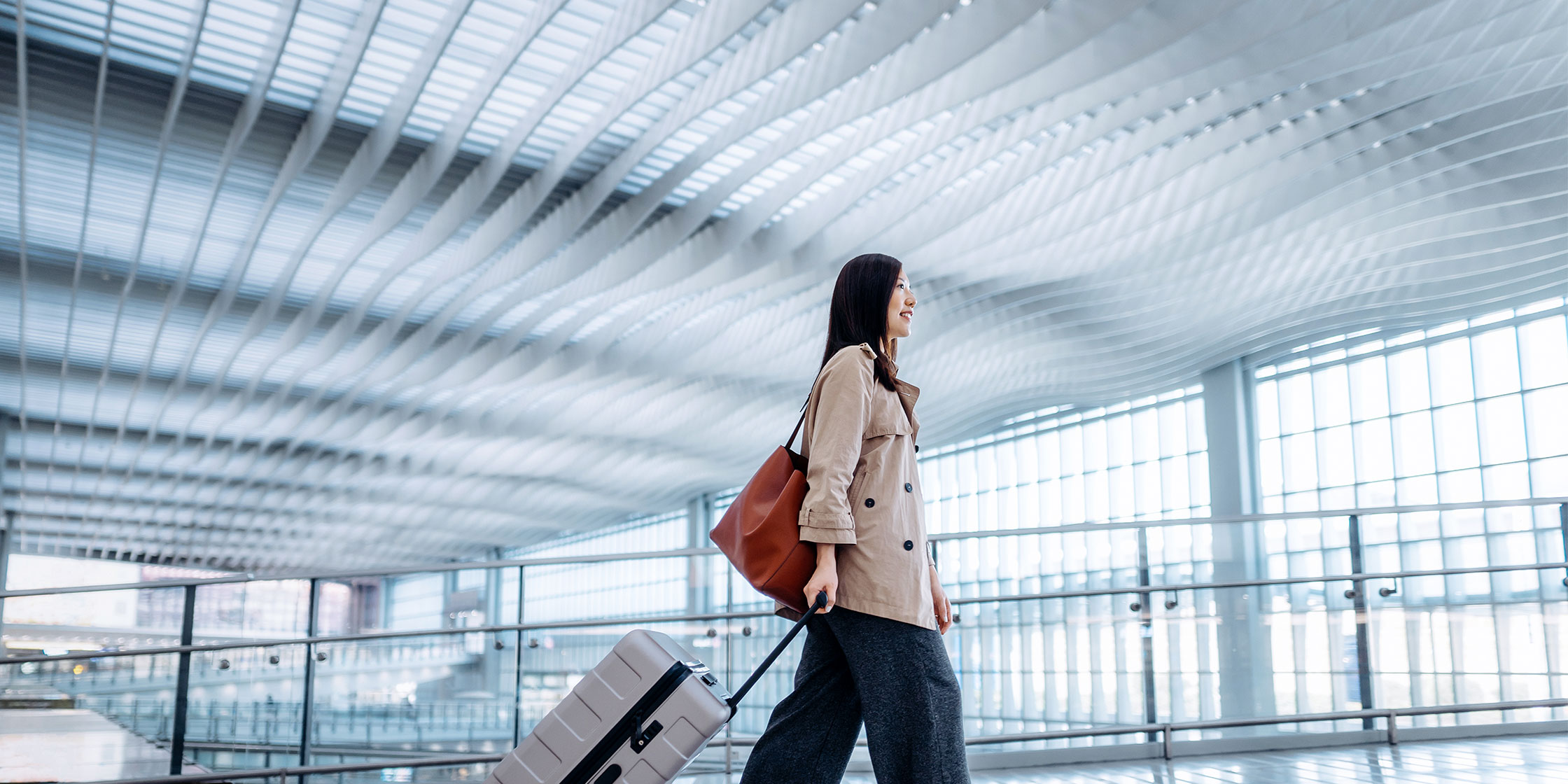 A person walks through an airport with their rolling luggage.