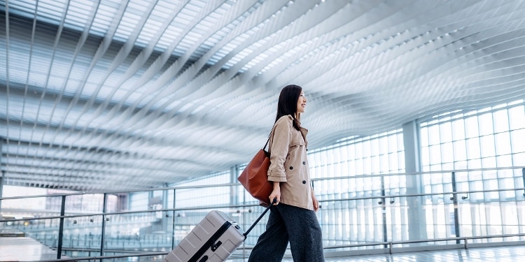 A person walks through an airport with their rolling luggage.