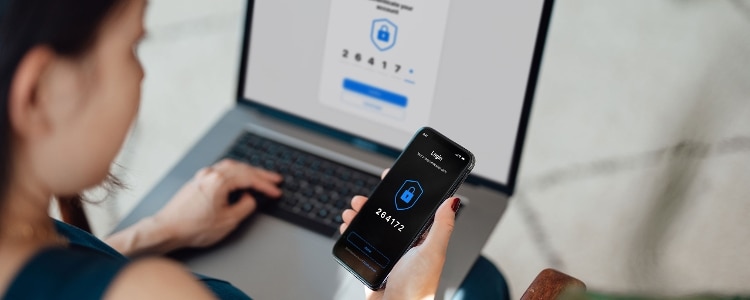 Someone signs in to an online account using their laptop and verifies their identity using two-factor authentication on their smartphone.