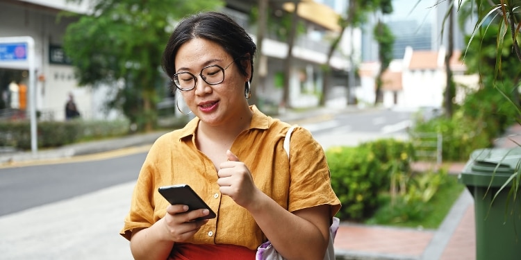 A person on a city sidewalk reading on their phone about credit cards with cellphone protection.
