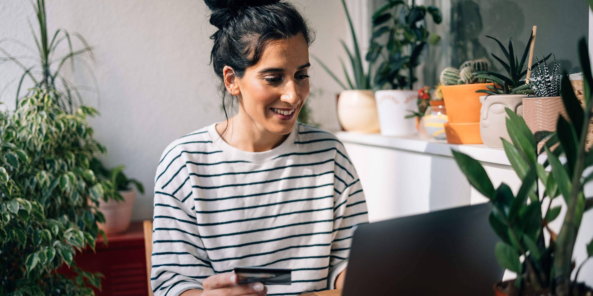 A person at home, surrounded by plants, uses an unsecured credit card to make a purchase online.