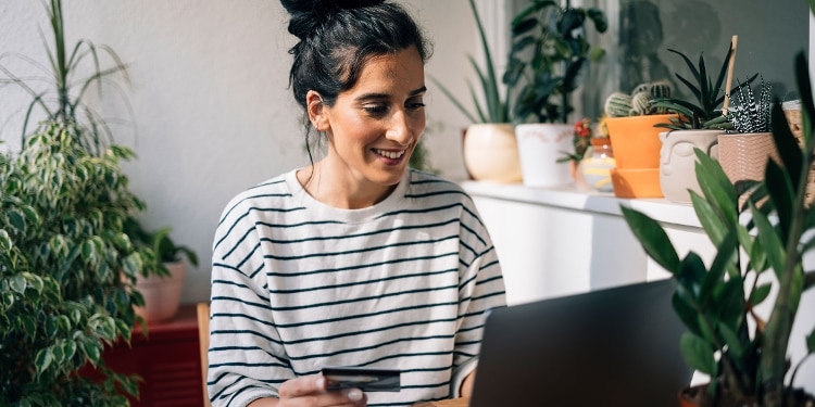 A person at home, surrounded by plants, uses an unsecured credit card to make a purchase online.