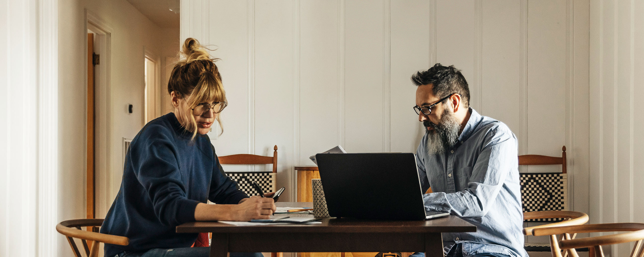A couple sit around a table at home with a laptop and paperwork to figure out their home expenses.