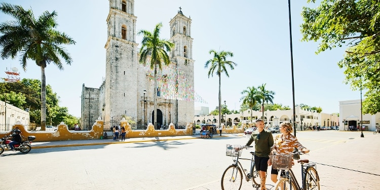 A man and a woman walk their bicycles through a historic Mexican town.