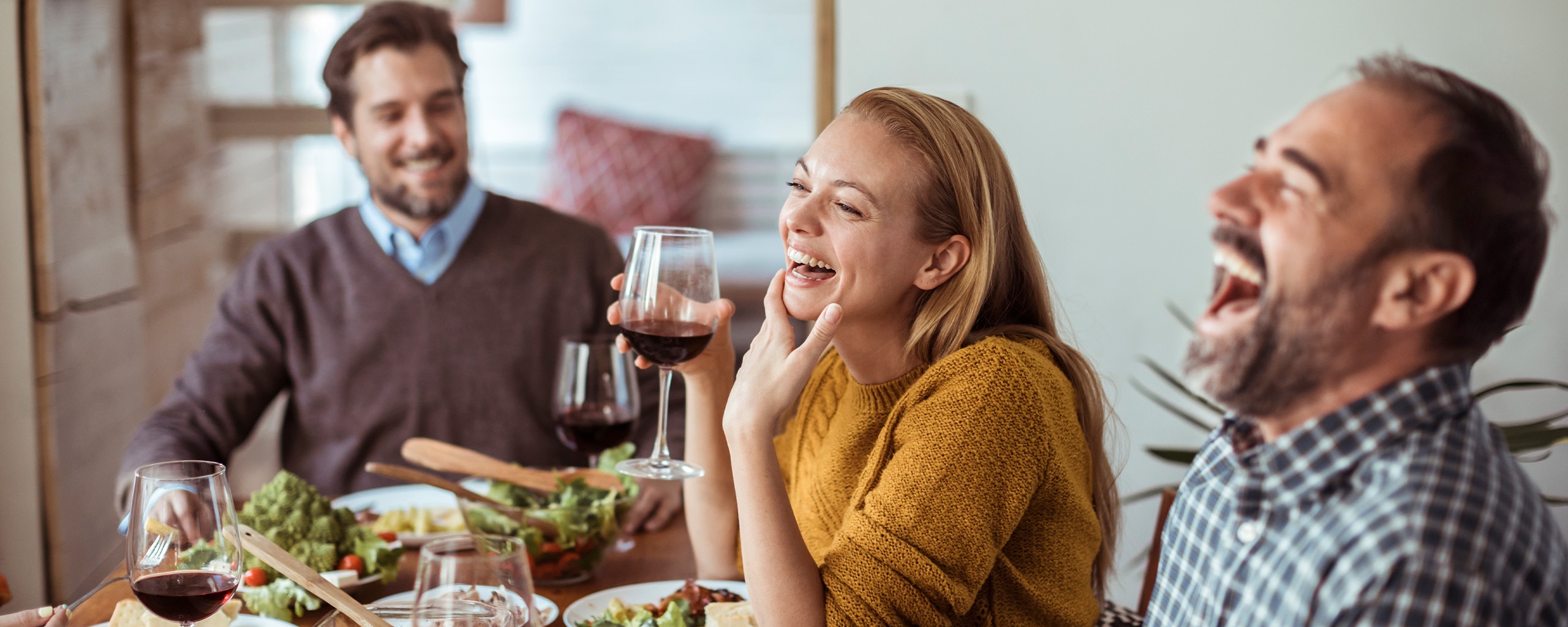 Three friends laugh while enjoying a holiday dinner.