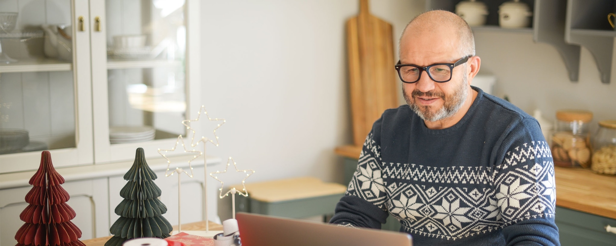 Person in a holiday sweater and glasses looks at their holiday budget on their laptop.