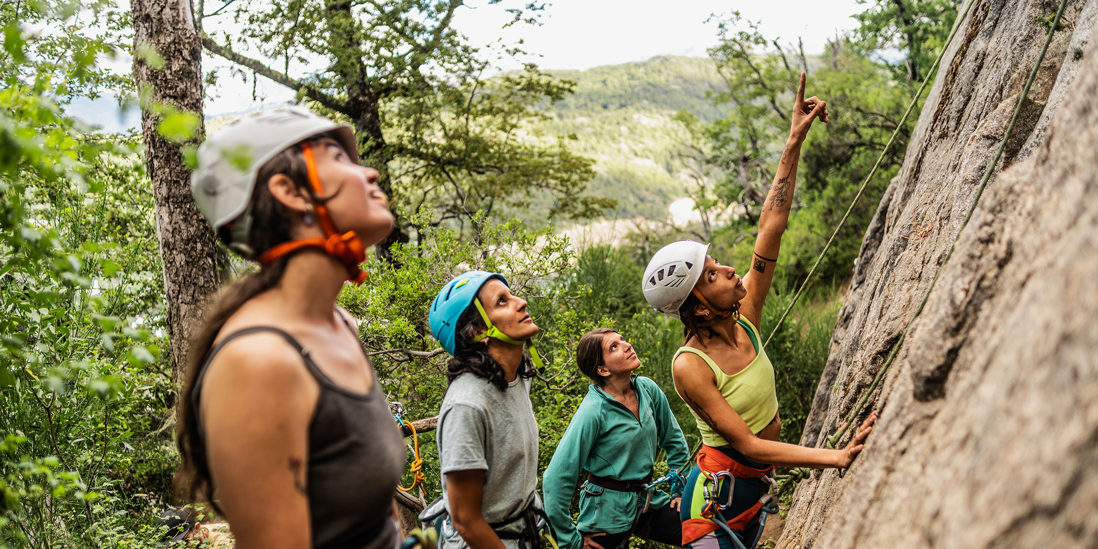 A group of friends in the woods wearing helmets and preparing to go rock climbing.