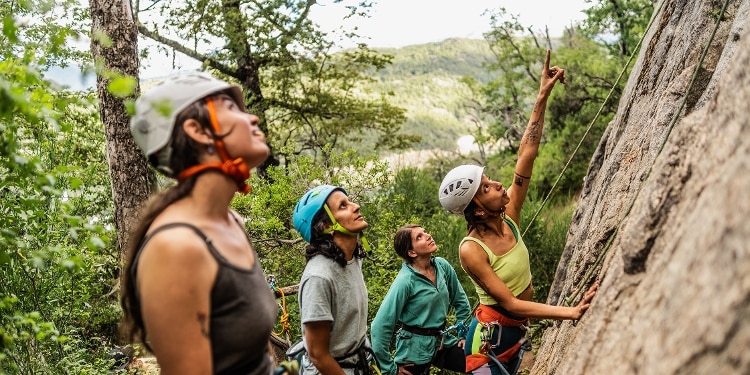 A group of friends in the woods wearing helmets and preparing to go rock climbing.