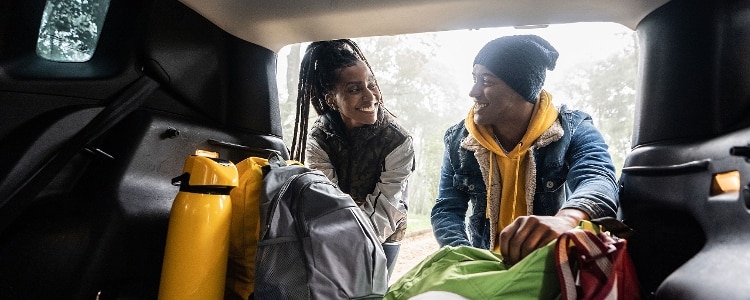Two people look at each other and smile as they load things into the back of a vehicle.