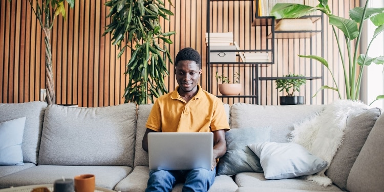 A person sits on a couch with his laptop open and researches open-end credit.