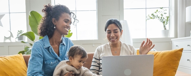 Two parents sit on a couch with their baby and use a laptop.