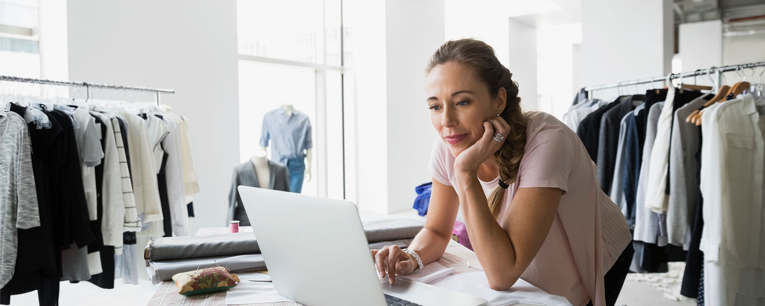 A person stands in their shop and uses their laptop to review their solo 401(k) account.
