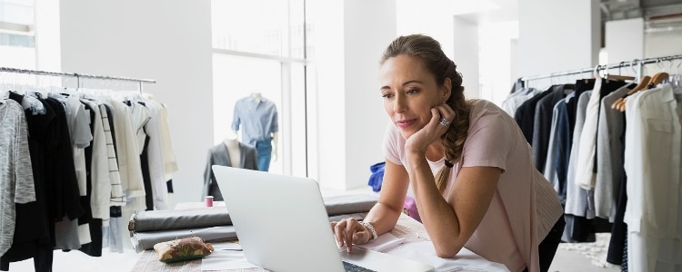 A person stands in their shop and uses their laptop to review their solo 401(k) account.&nbsp;
